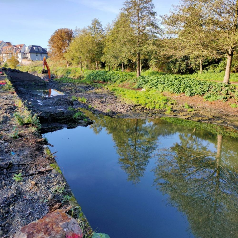 Cours d'eau entouré de végétation au premier plan, avec des engins de chantier en arrière-plan - Navarra TS