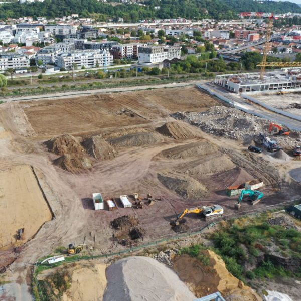 Photo aérienne par drone d'un chantier, plusieurs engins autour d'un grand terrain sur lequel se trouvent plusieurs tas de terre